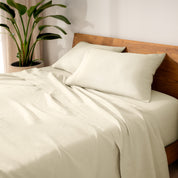 Linen bed sheets and pillows on a wooden bed with a plant in the background