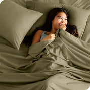 A smiling woman on a bed with a microfiber sheet over her