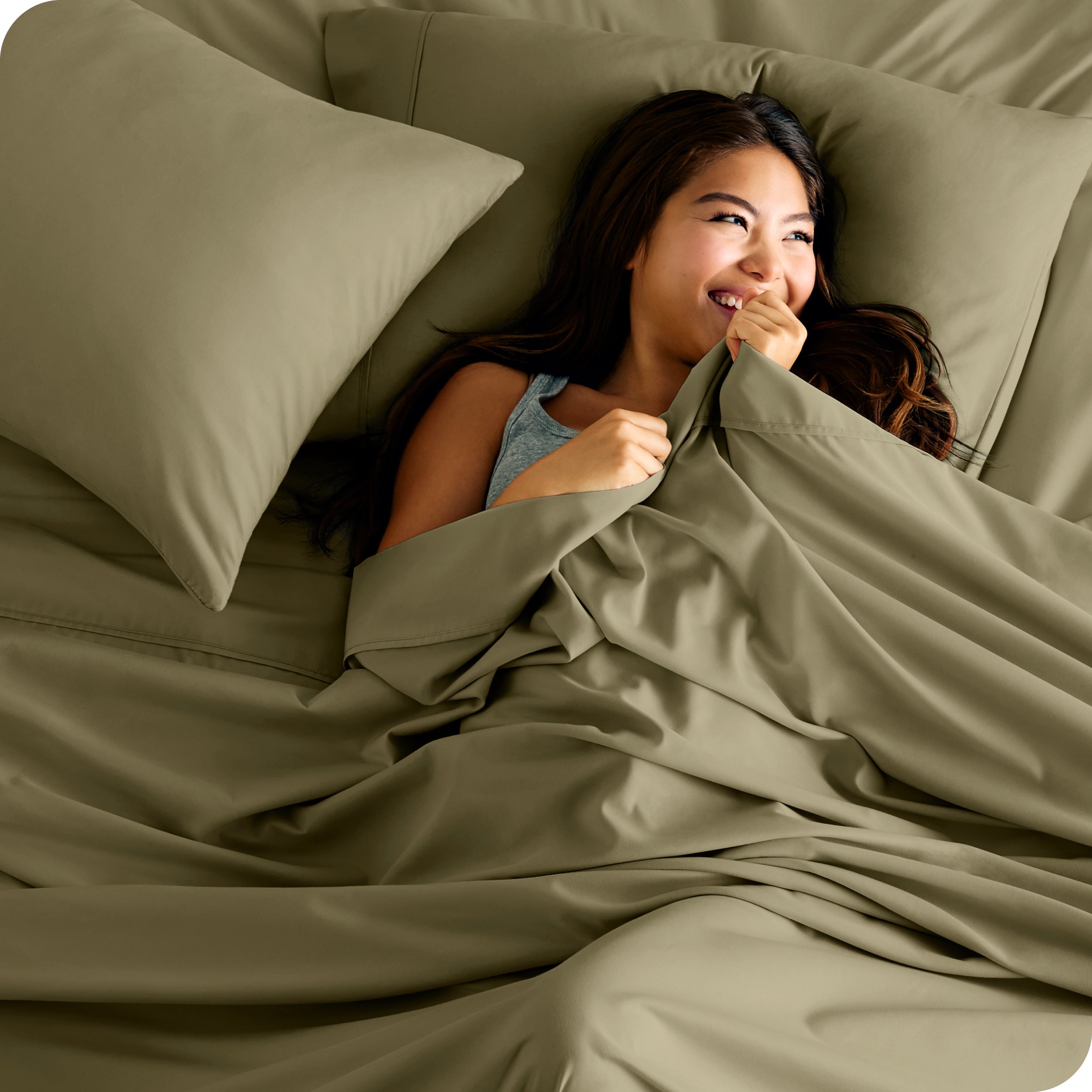 A smiling woman on a bed with a microfiber sheet over her