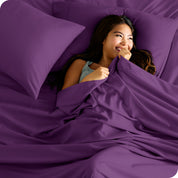 A smiling woman on a bed with a microfiber sheet over her