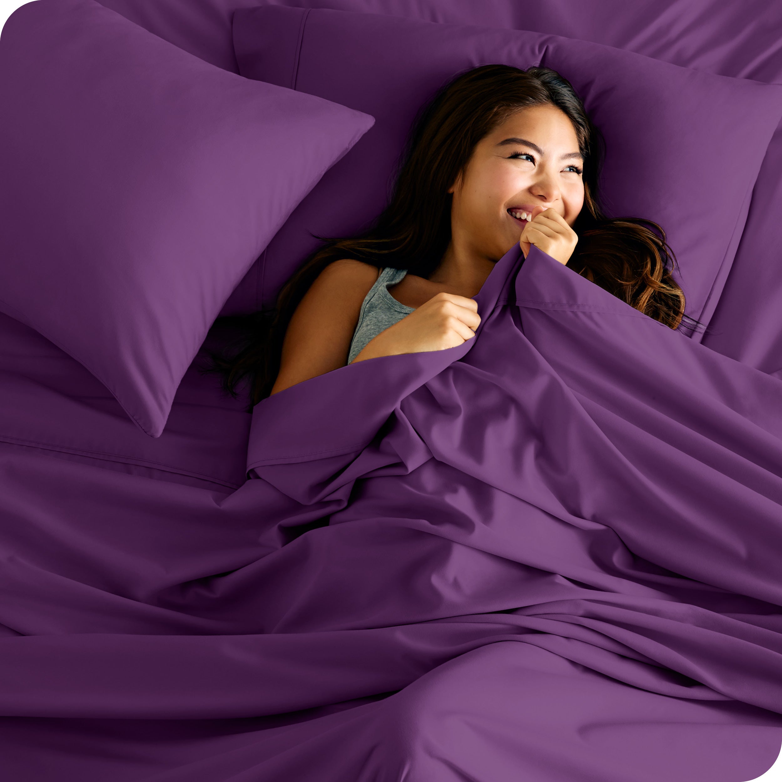 A smiling woman on a bed with a microfiber sheet over her