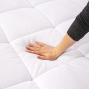 A hand is feeling the texture of the mattress pad.