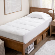 A reversible mattress pad on a bed with a wooden headboard .