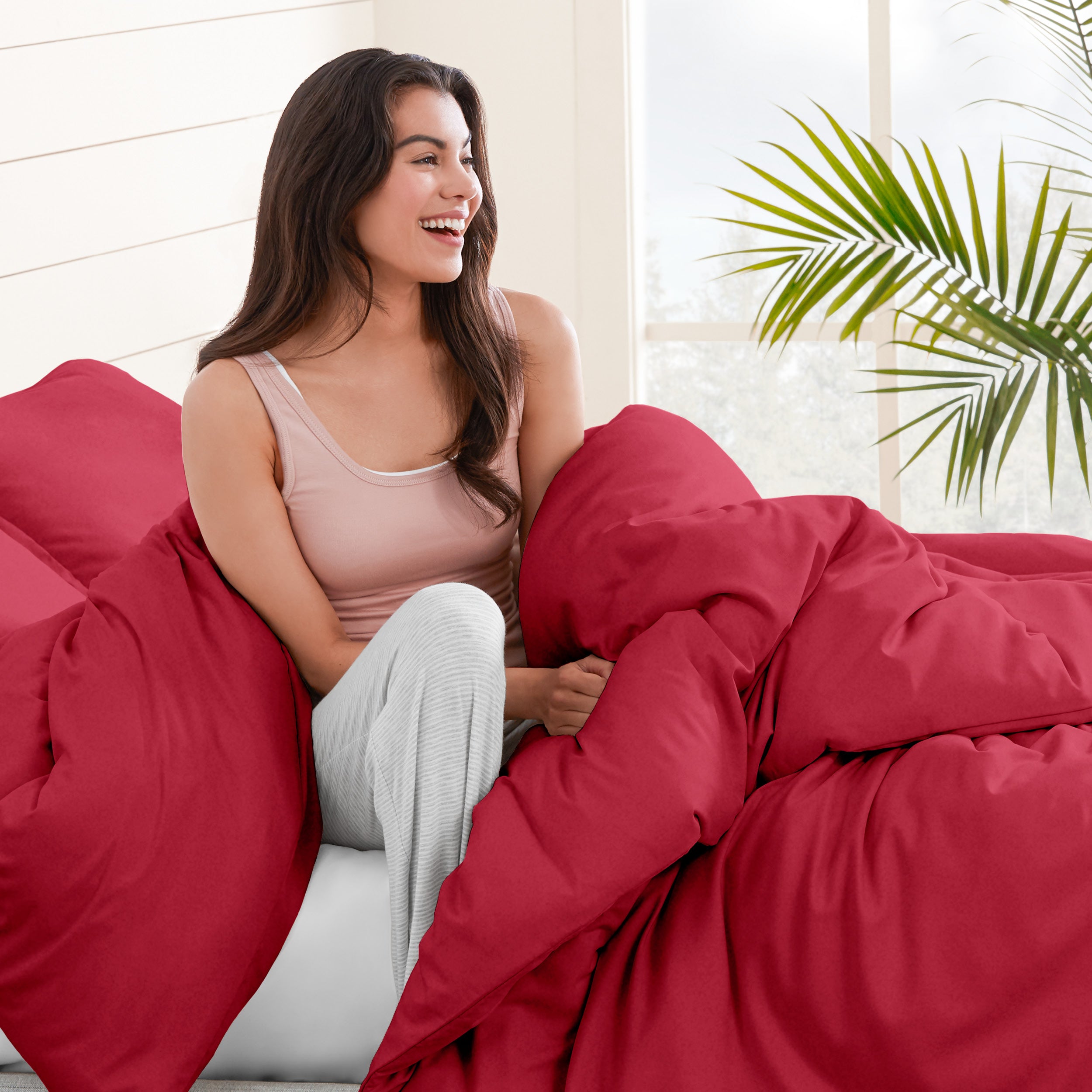 A woman sitting on a bed, wrapped in a comforter featuring the Bare Home flannel duvet set.