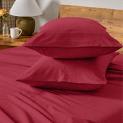 Two pillows with flannel pillowcases stacked on a bed with a wooden headboard and side table in the background.