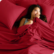 A smiling woman on a bed with a microfiber sheet over her