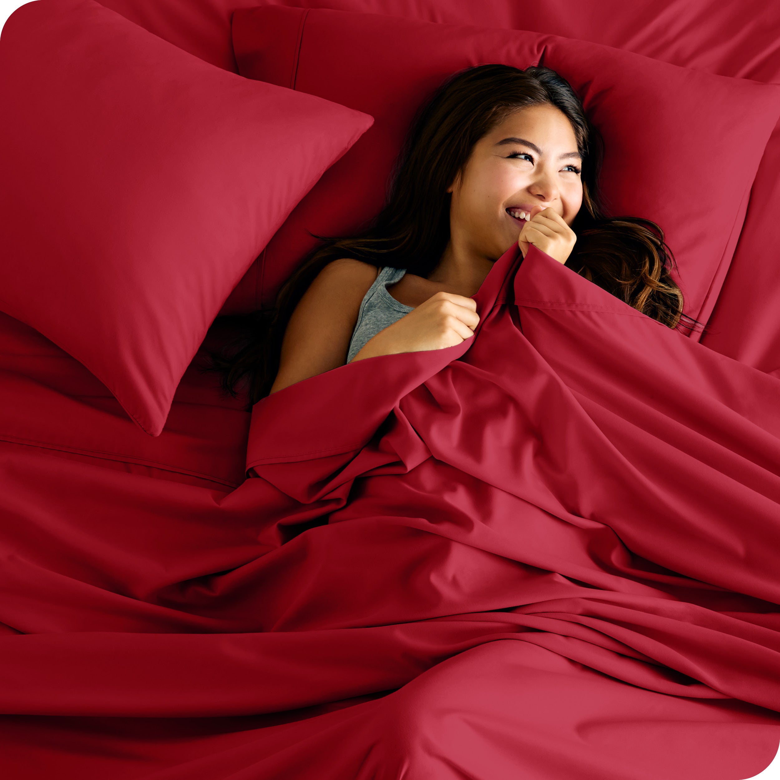A smiling woman on a bed with a microfiber sheet over her