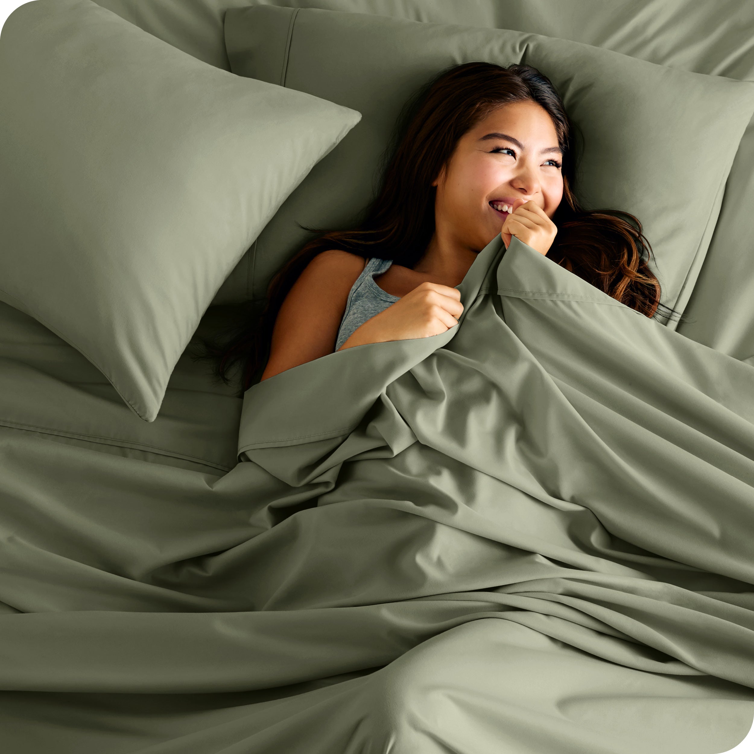 A smiling woman on a bed with a microfiber sheet over her