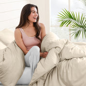 A woman sitting on a bed, wrapped in a comforter featuring the Bare Home flannel duvet set.