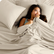 A smiling woman on a bed with a microfiber sheet over her