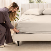 A woman is putting a fitted sheet on a mattress