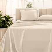 Organic sateen bedding on a bed with a beige headboard and plant in the corner.