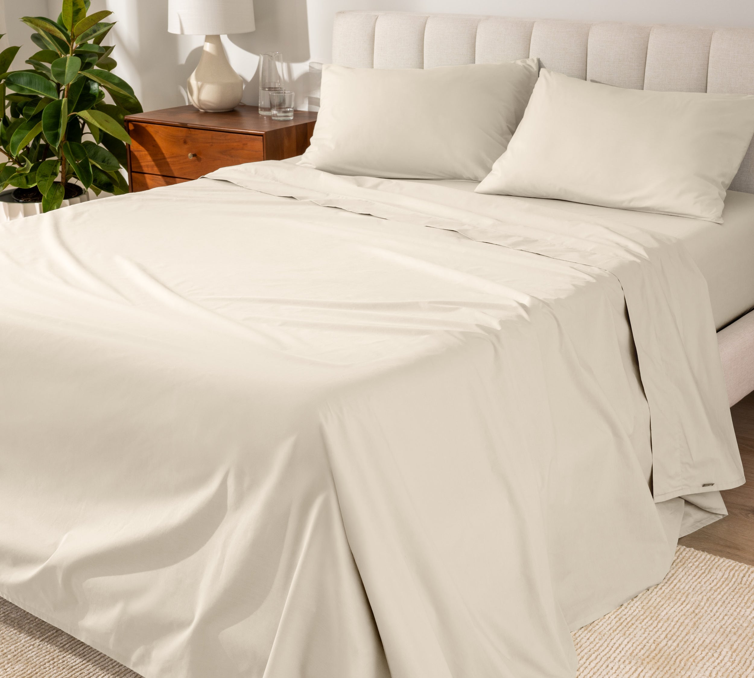 Organic cotton percale sheet set on a bed, with a flat sheet, fitted sheet, and two pillowcases displayed.