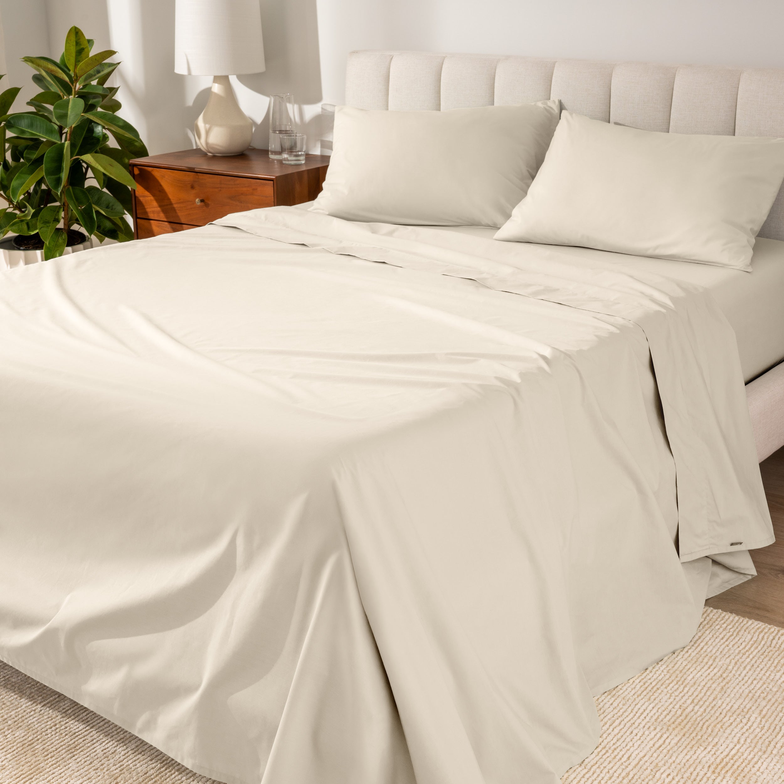Organic cotton percale sheet set on a bed, with a flat sheet, fitted sheet, and two pillowcases displayed.