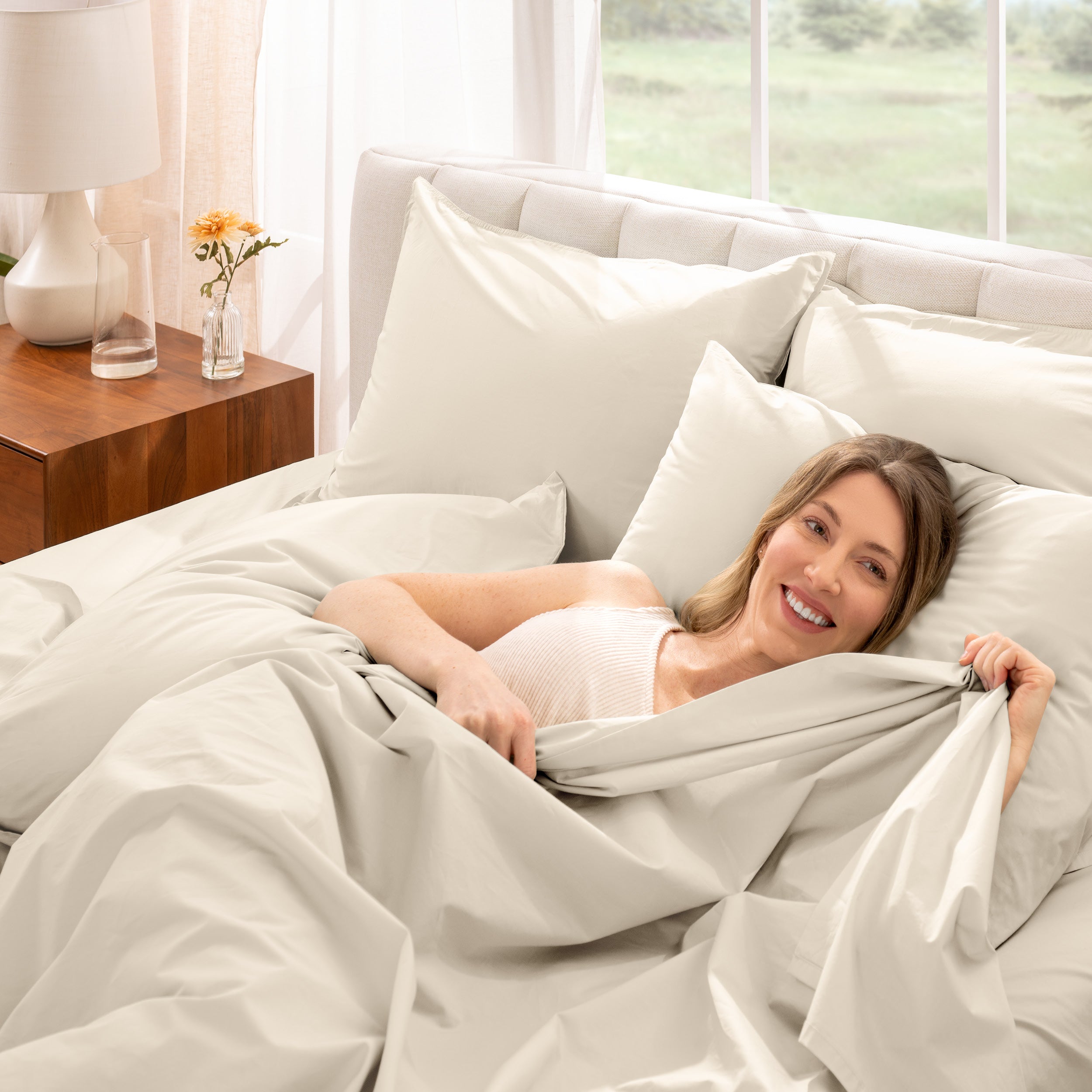 Woman lying in bed under percale sheets with a bright room setting