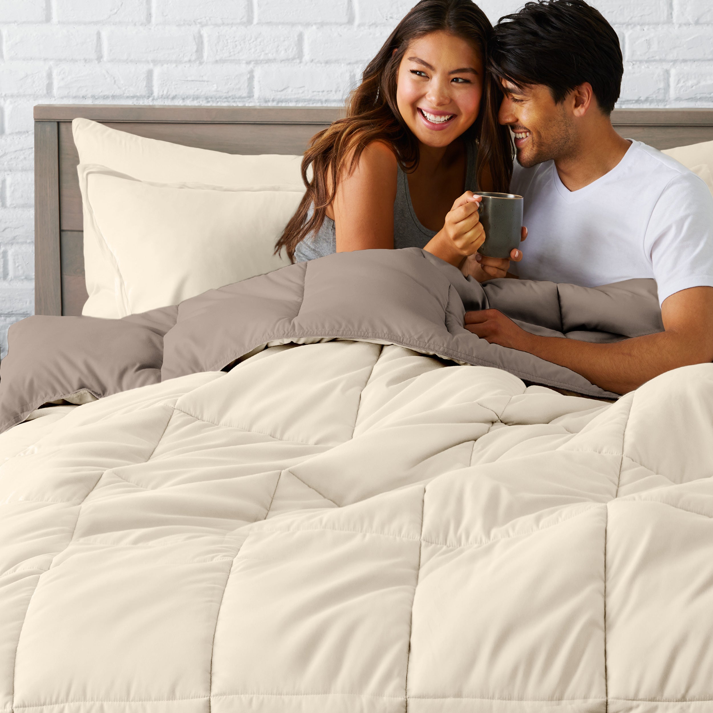 A couple sitting in a bed made with a reversible comforter and sheet set