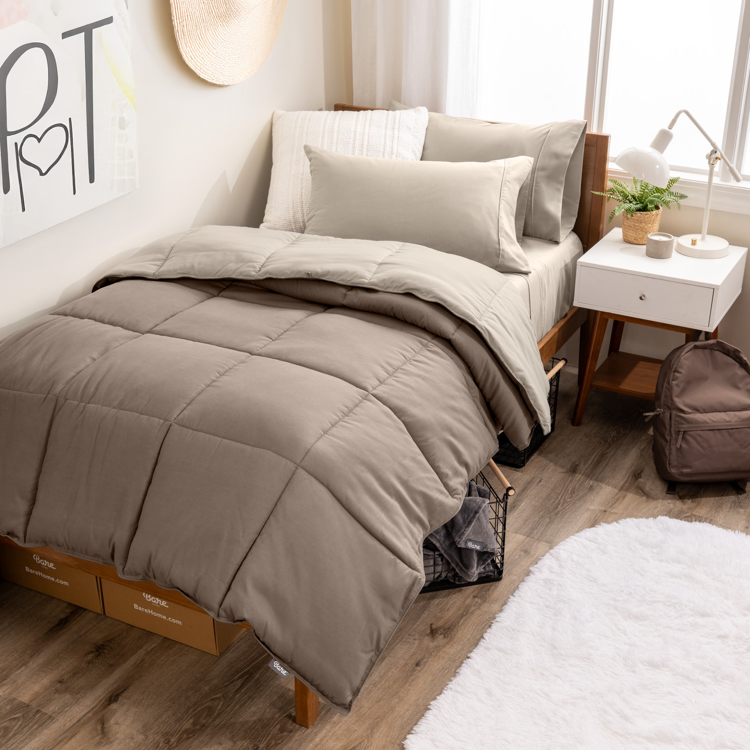 A wooden bed frame with a reversible comforter and sheet set on the mattress in a dorm style room.