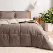 A wooden bed frame with a reversible comforter and sheet set on the mattress in a bright warm room.