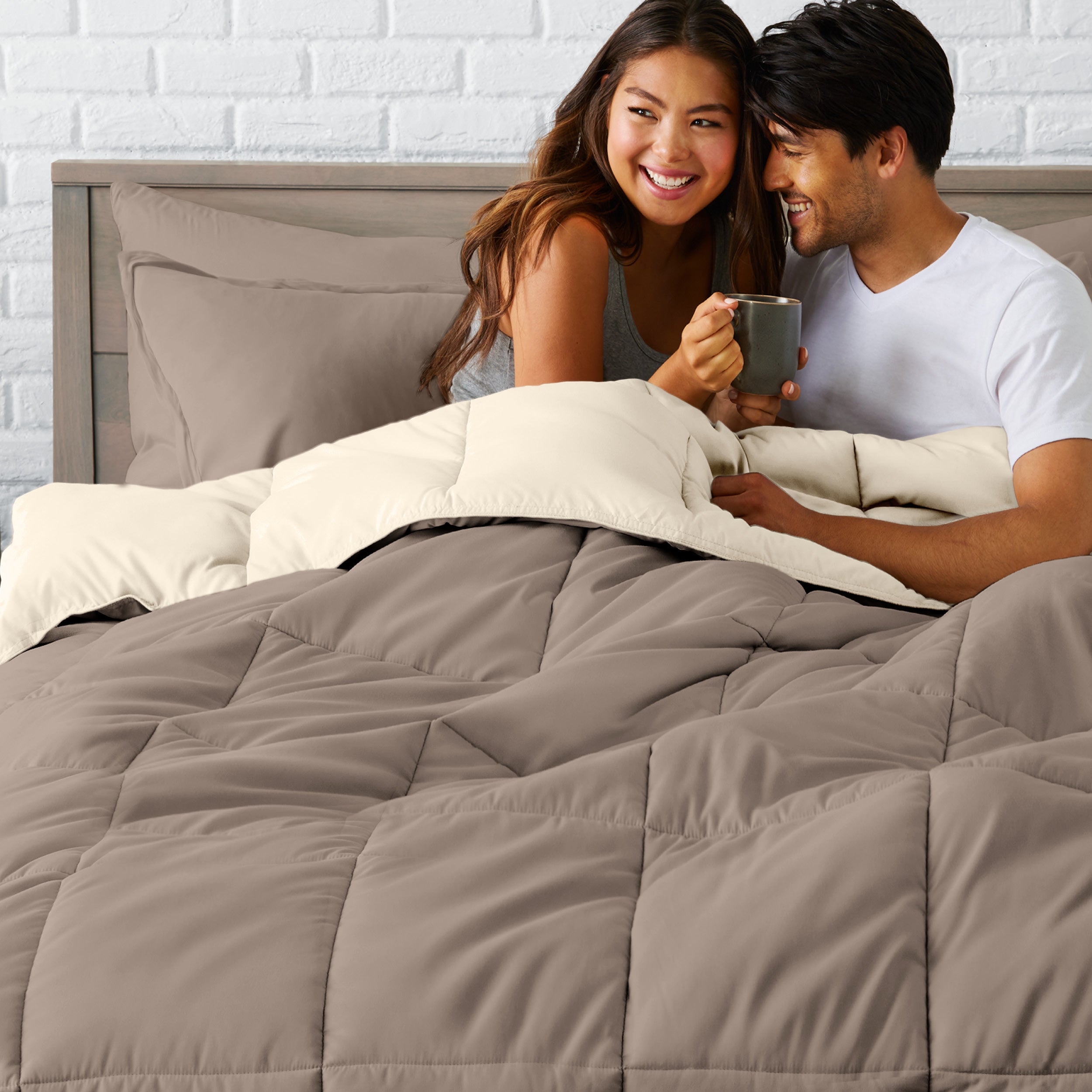 A couple sitting in a bed made with a reversible comforter and sheet set