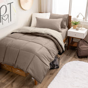 A wooden bed frame with a reversible comforter and sheet set on the mattress in a dorm style room.