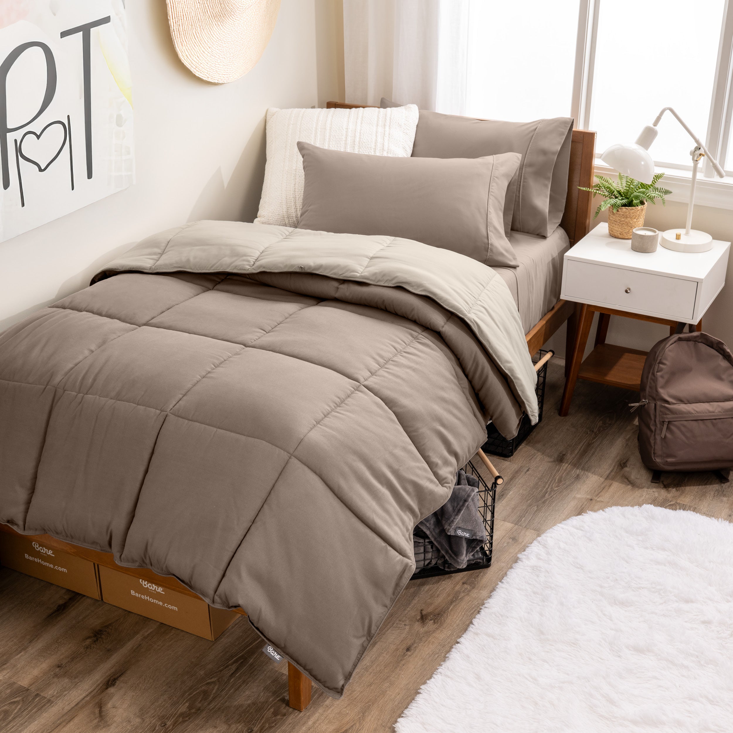 A wooden bed frame with a reversible comforter and sheet set on the mattress in a dorm style room.