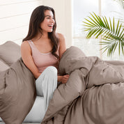 A woman sitting on a bed, wrapped in a comforter featuring the Bare Home flannel duvet set.