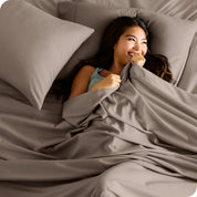 A smiling woman on a bed with a microfiber sheet over her