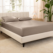 Organic cotton fitted sheet on a bed in a bedroom with a plant and window in the background