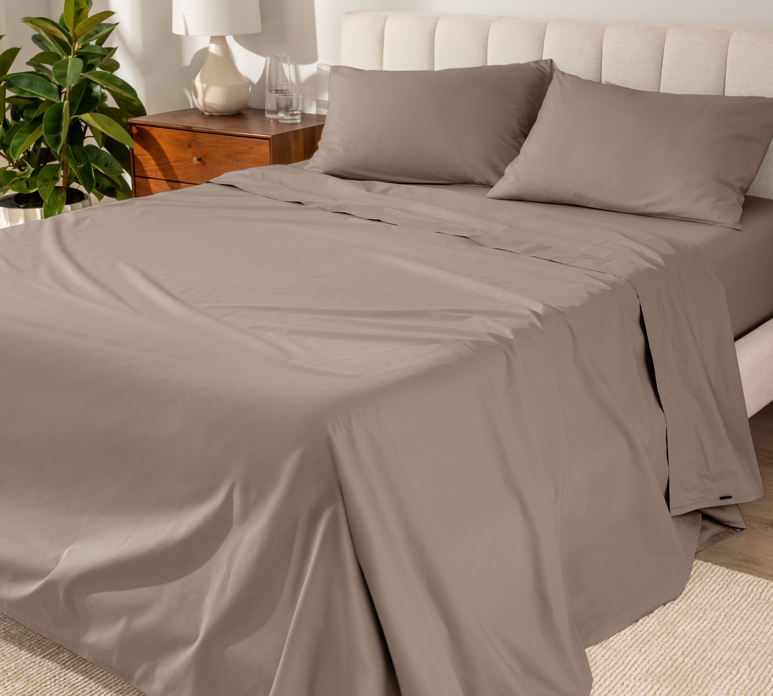 Organic cotton percale sheet set on a bed, with a flat sheet, fitted sheet, and two pillowcases displayed.