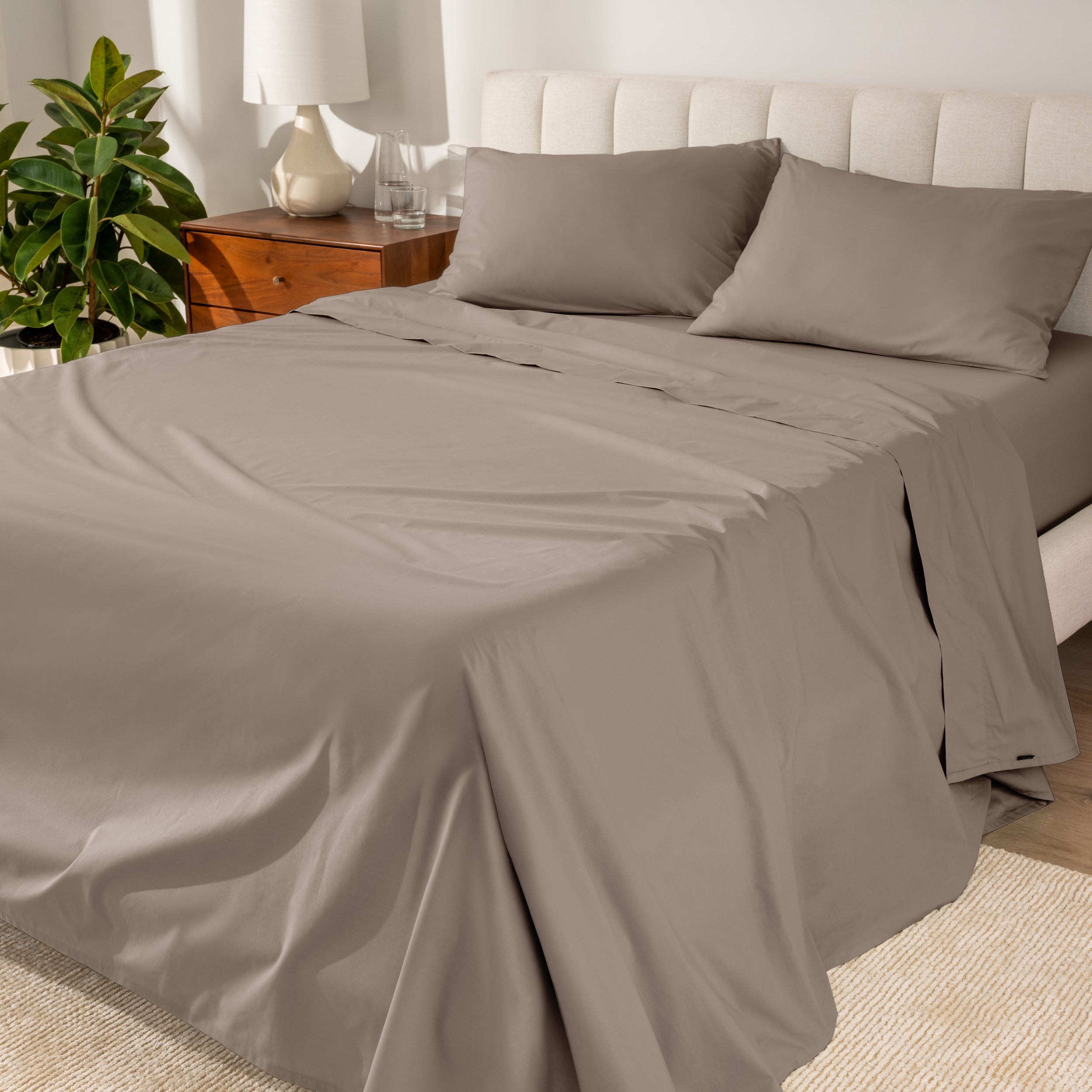 Organic cotton percale sheet set on a bed, with a flat sheet, fitted sheet, and two pillowcases displayed.