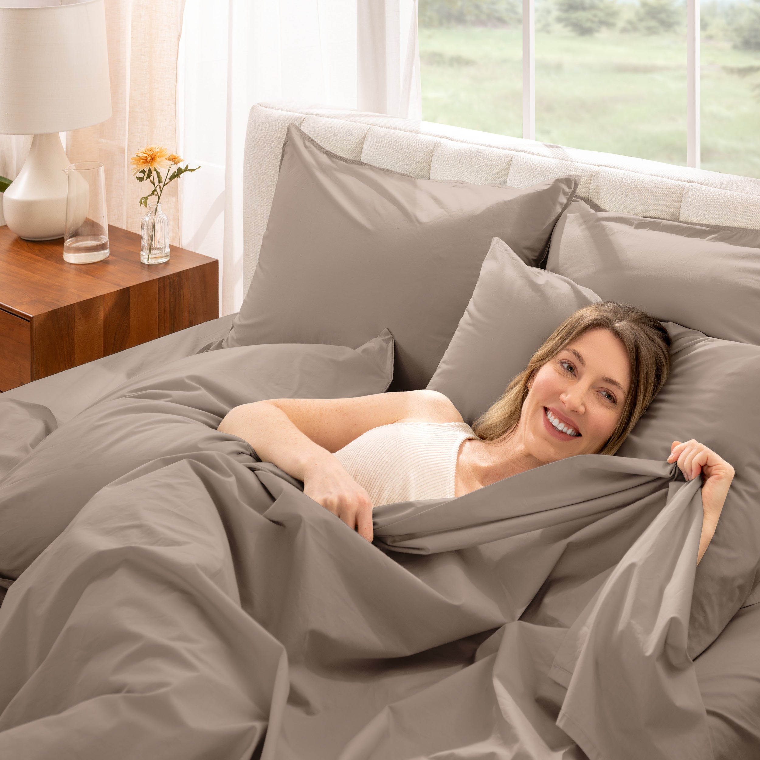 Woman lying in bed under percale sheets with a bright room setting