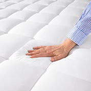 A hand is feeling the soft cotton texture of the mattress pad.