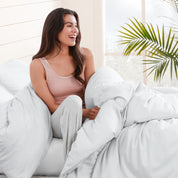 A woman sitting on a bed, wrapped in a comforter featuring the Bare Home flannel duvet set.
