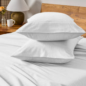 Two pillows with flannel pillowcases stacked on a bed with a wooden headboard and side table in the background.