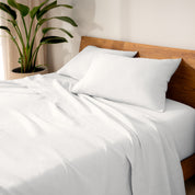 Linen bed sheets and pillows on a wooden bed with a plant in the background