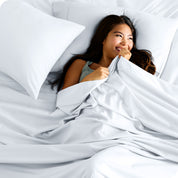 A smiling woman on a bed with a microfiber sheet over her