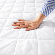 A hand is feeling the texture of the mattress pad.