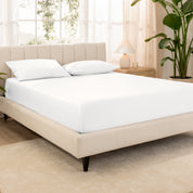 Organic cotton fitted sheet on a bed in a bedroom with a plant and window in the background