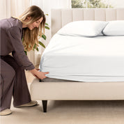 A woman is putting a fitted sheet on a mattress