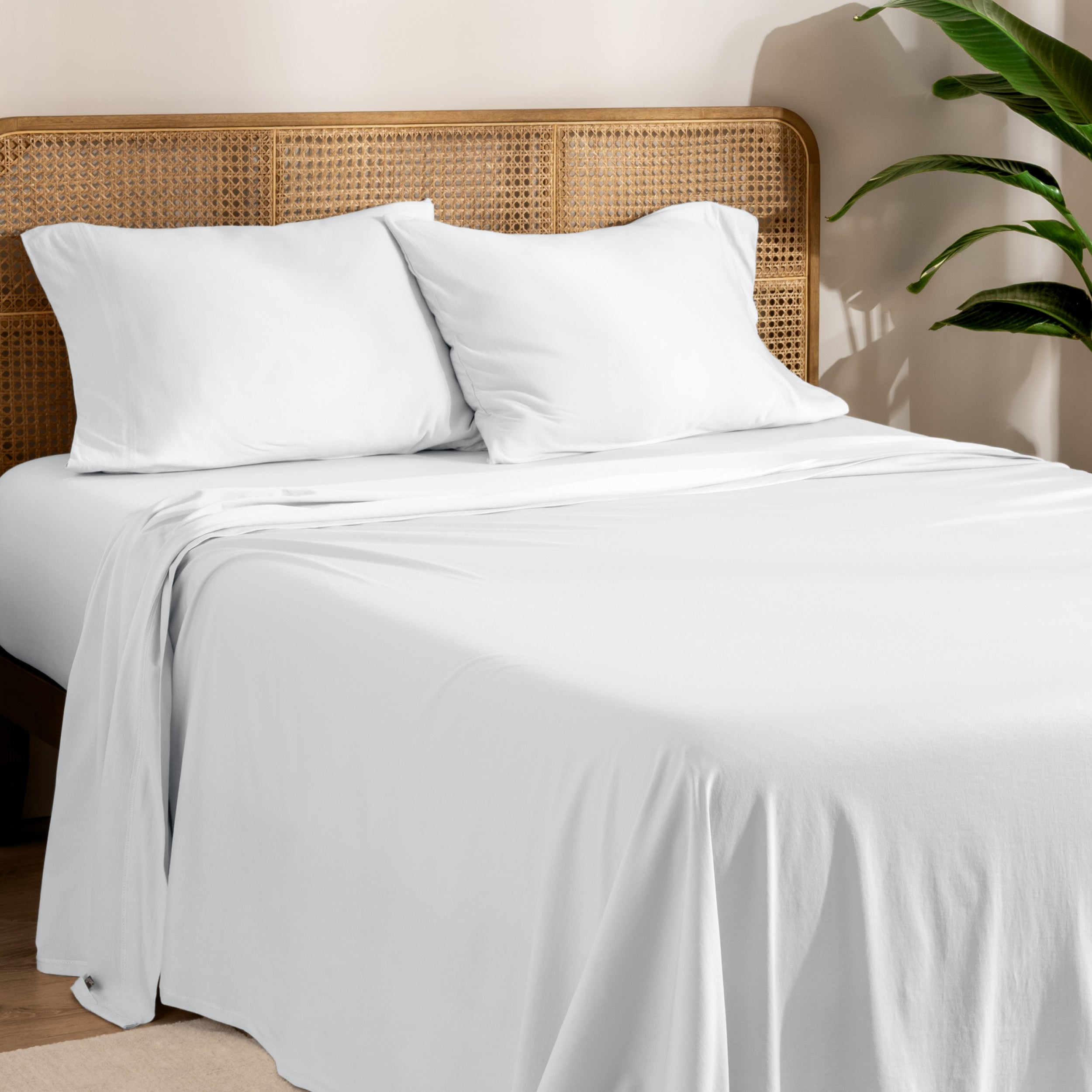 Organic jersey sheets and pillowcases on a bed with plants on the side in a bright and chill room scene.