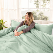 A woman sitting on a bed made with organic cotton sateen sheets and pillowcases