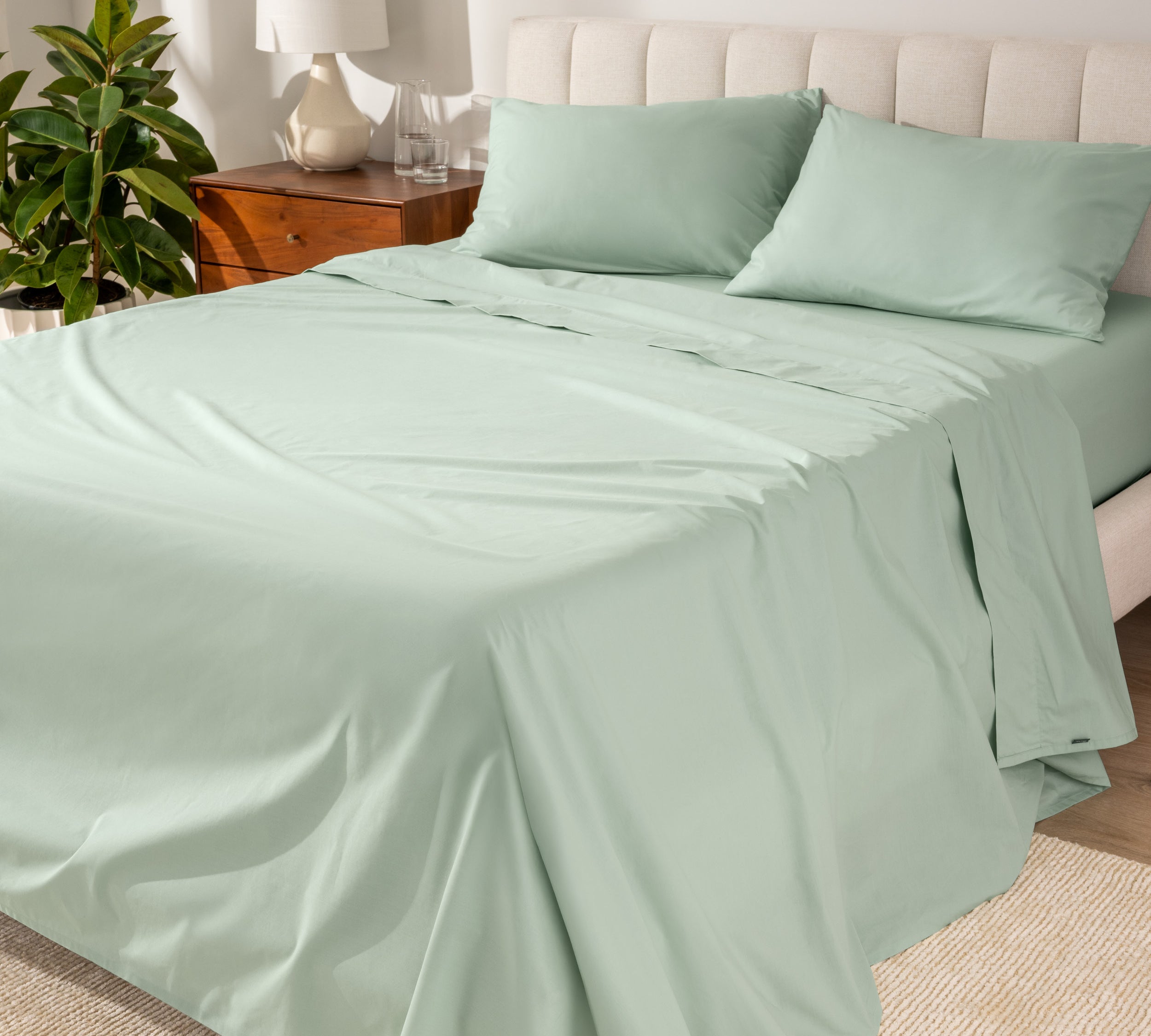 Organic cotton percale sheet set on a bed, with a flat sheet, fitted sheet, and two pillowcases displayed.