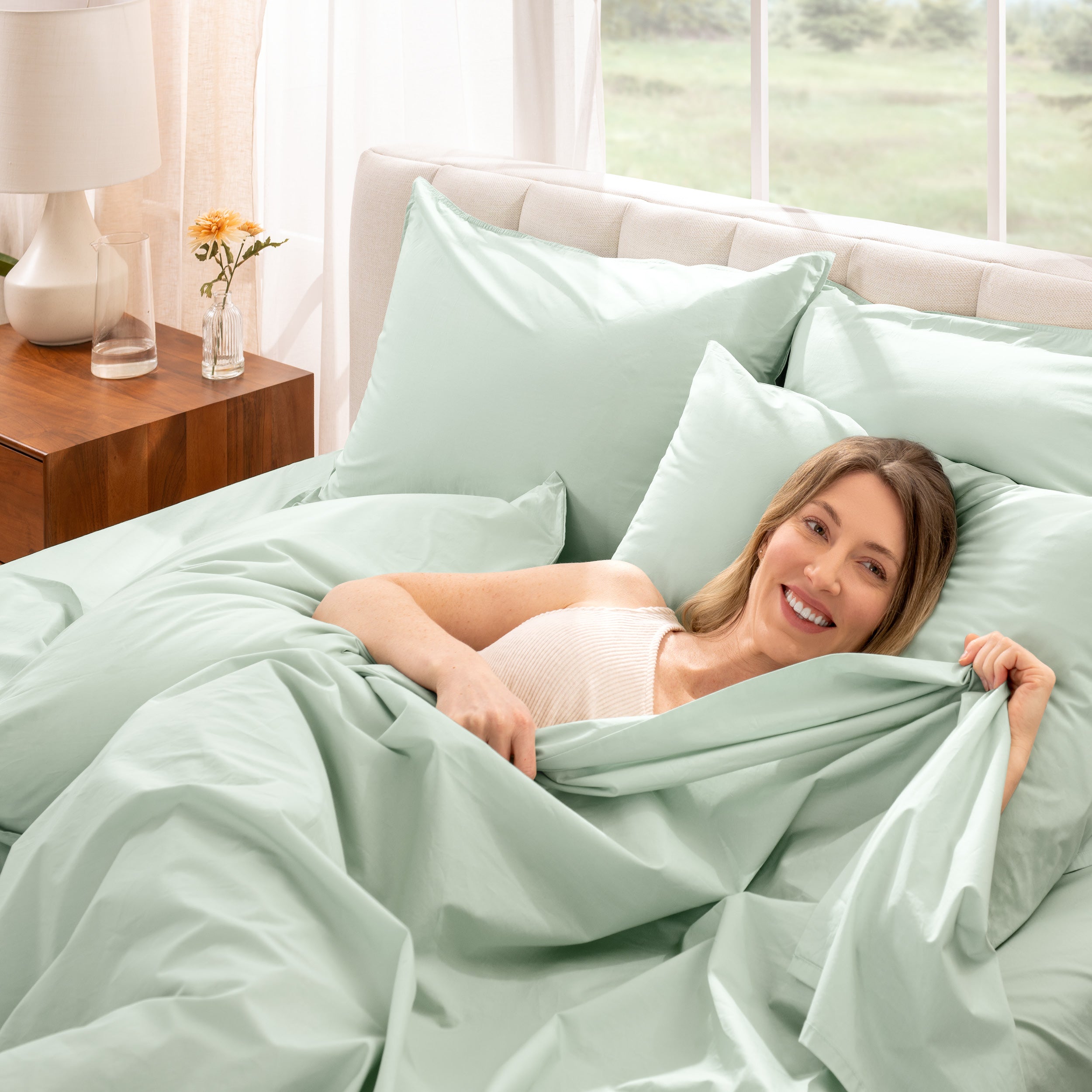 Woman lying in bed under percale sheets with a bright room setting