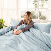 A woman sitting on a bed made with organic cotton sateen sheets and pillowcases