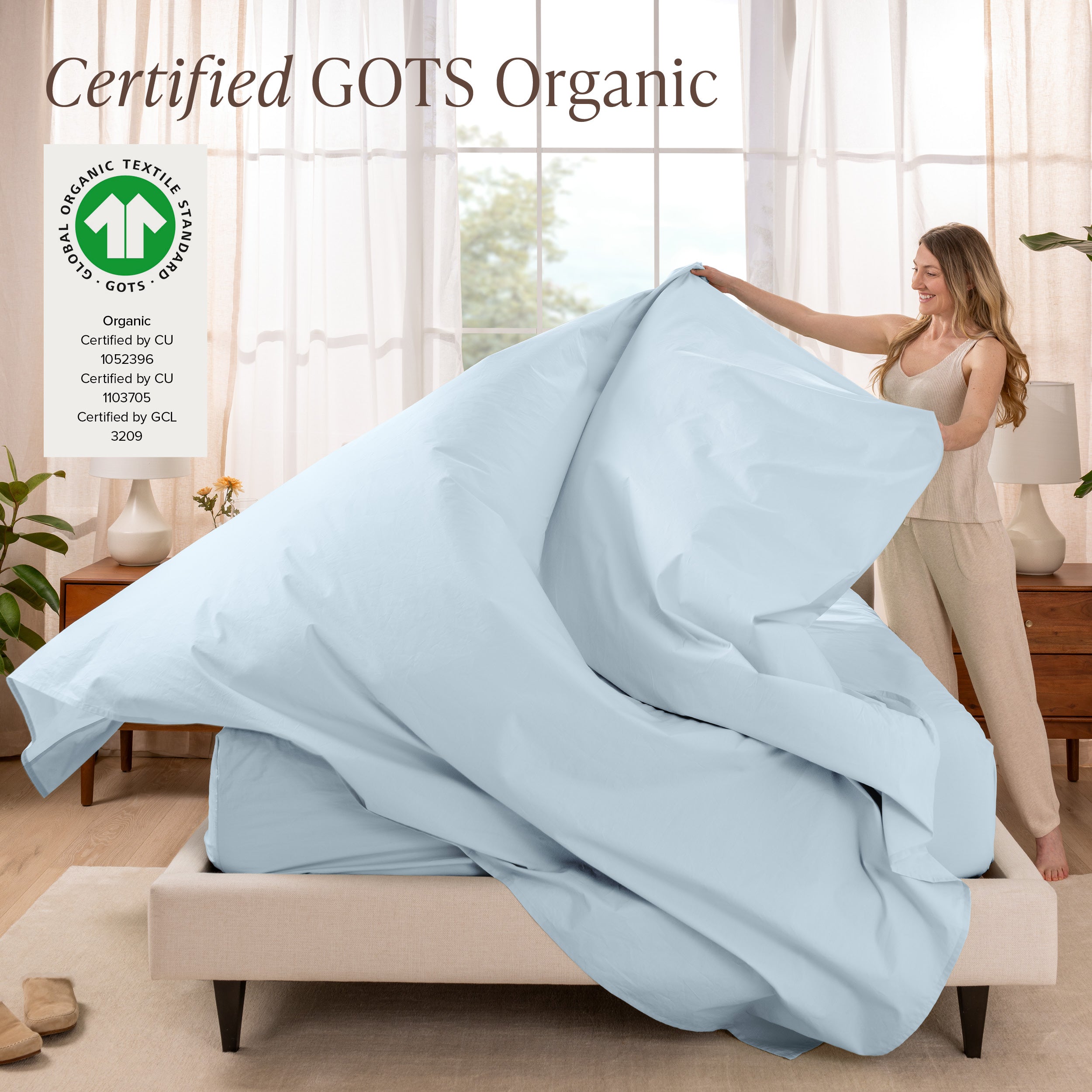 Woman putting bedding on a bed with GOTS Organic certification logo in the corner.
