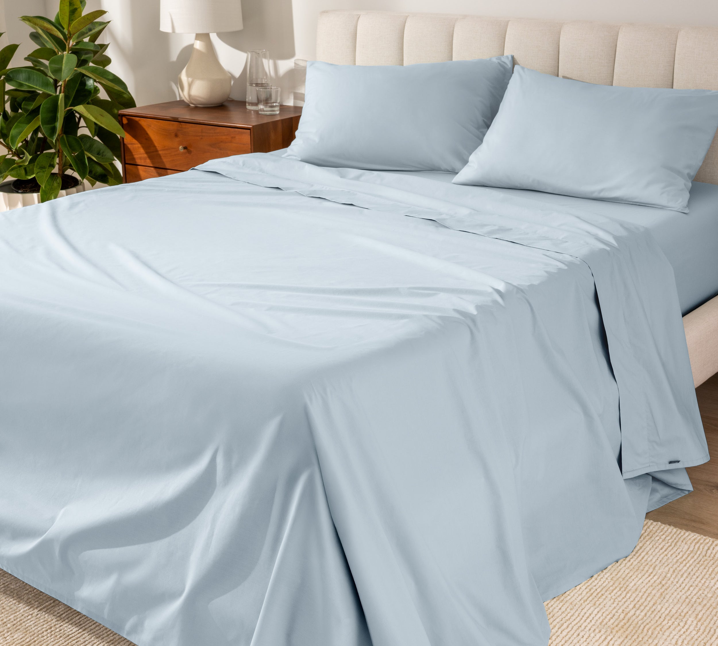 Organic cotton percale sheet set on a bed, with a flat sheet, fitted sheet, and two pillowcases displayed.