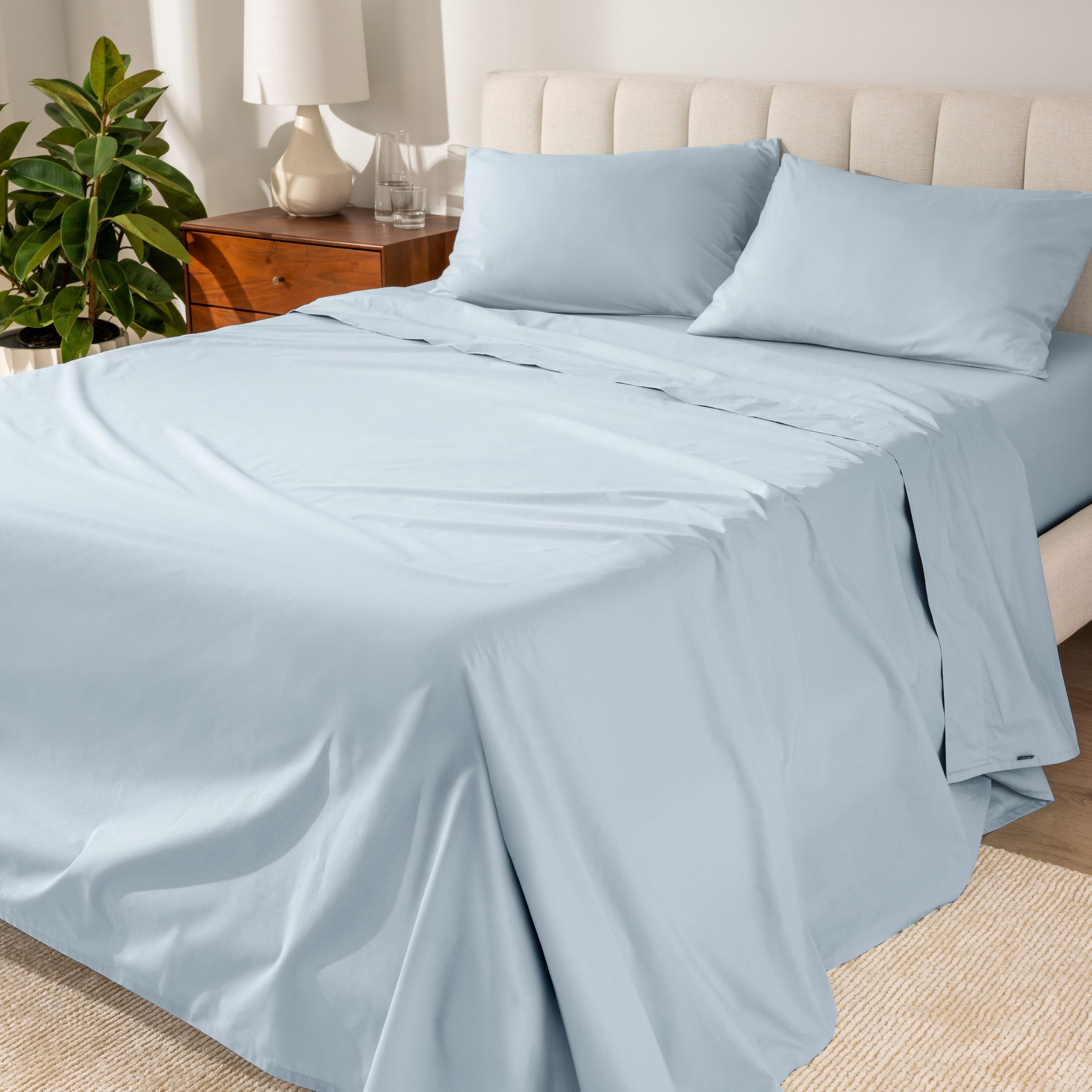 Organic cotton percale sheet set on a bed, with a flat sheet, fitted sheet, and two pillowcases displayed.