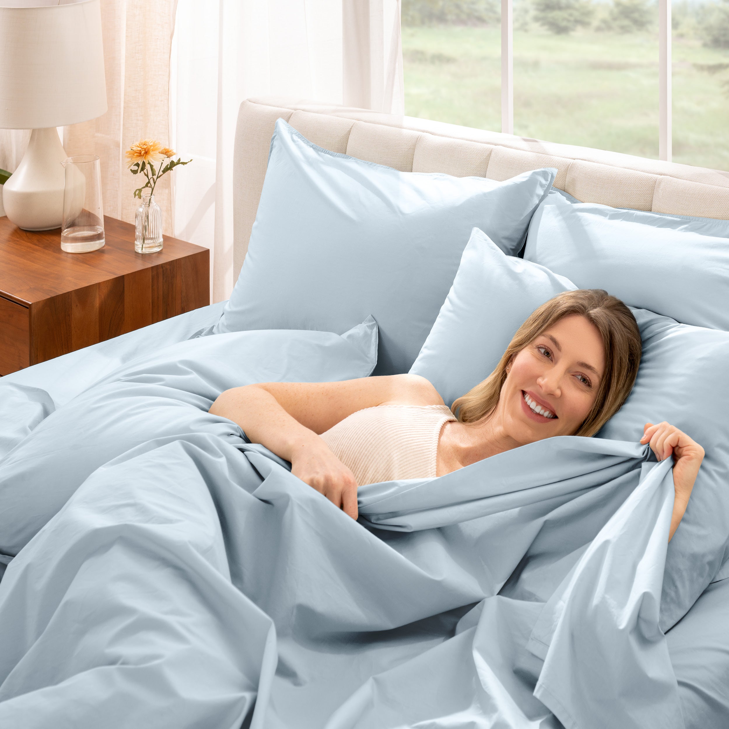 Woman lying in bed under percale sheets with a bright room setting