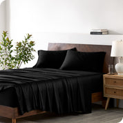 Modern bedroom with a bed against a white wall with a nightstand next to the bed. The bed has bamboo sheets draped over it.