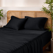 Bamboo bed sheets and pillowcases on a bed with a wicker headboard and plants in the background.